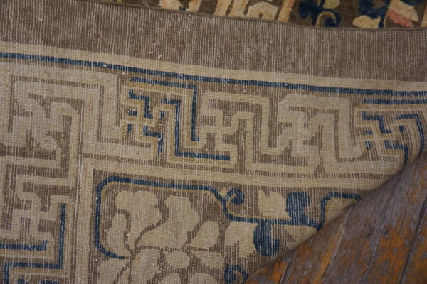 Low-pile rug corner featuring tan, brown, and blue geometric and floral patterns on wood floors.