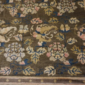 Dark olive-brown rug with beige, pink, and blue florals and a Greek key patterned border.