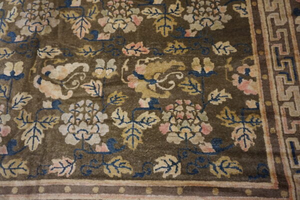 Dark olive-brown rug with beige, pink, and blue florals and a greek key patterned border.