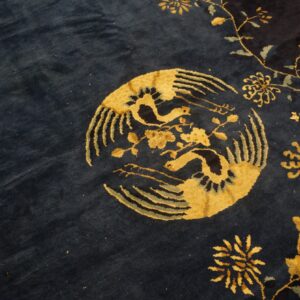 Navy blue plush rug with a gold circular bird and floral vine pattern detail.