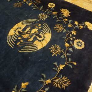 Navy rug with golden yellow birds and flower vines rests on bright wooden plank flooring.