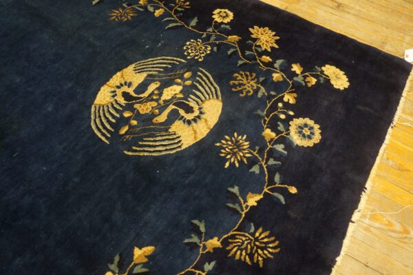 Navy rug with golden yellow birds and flower vines rests on bright wooden plank flooring.