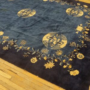 High-pile blue rug with a gold floral and bird medallion pattern lying on worn hardwood flooring.