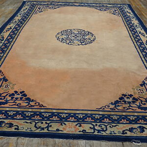 Low-pile rug in peach and navy blue with ornate corner motifs displayed on distressed wood flooring.
