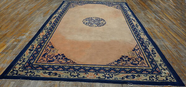 Low-pile rug in peach and navy blue with ornate corner motifs displayed on distressed wood flooring.