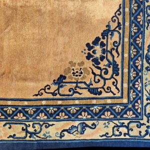 Close-up of a high pile tan rug corner with detailed deep blue and pale beige floral borders.