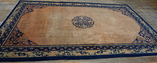 Rectangular low-pile rug featuring a peach field and intricate navy blue traditional borders on wood floors.