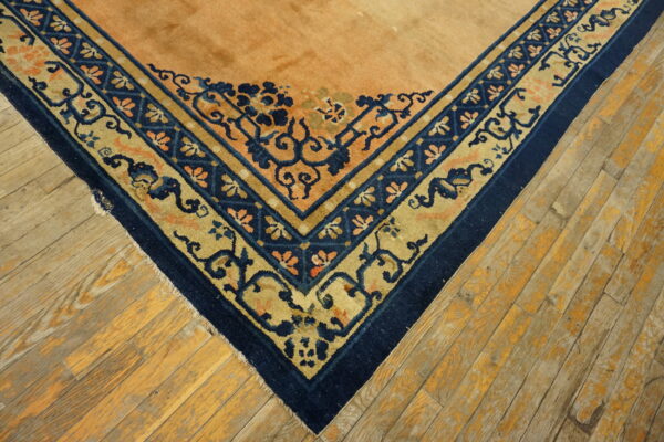 Intricate navy blue and gold bordered rug corner rests on rustic, worn wood flooring.