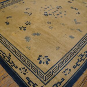 Gold rug with scattered blue botanical motifs and a thick blue border with a Greek key design on wood planks.