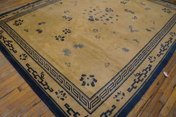 Gold rug with scattered blue botanical motifs and a thick blue border with a greek key design on wood planks.