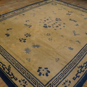 A large tan rug with scattered blue floral patterns and an ornate blue geometric border on a wooden floor.