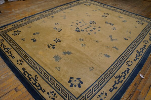 A large tan rug with scattered blue floral patterns and an ornate blue geometric border on a wooden floor.