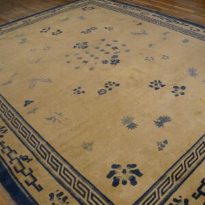 Tan rug with scattered blue floral motifs and a Greek key border rests on wood planks.