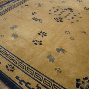 Golden low-pile rug with a wide dark blue geometric border and scattered blue floral designs on wood flooring.