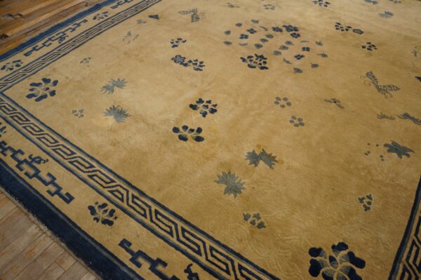 Golden low-pile rug with a wide dark blue geometric border and scattered blue floral designs on wood flooring.