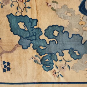 Detail of a cream rug featuring large teal and gray cloud patterns, small birds, and blue floral branches.