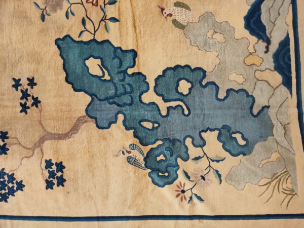 Detail of a cream rug featuring large teal and gray cloud patterns, small birds, and blue floral branches.