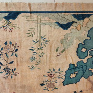 A plush tan rug featuring a detailed nature pattern in teal, green, and blue.