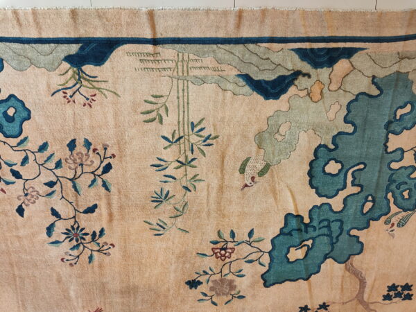 A plush tan rug featuring a detailed nature pattern in teal, green, and blue.