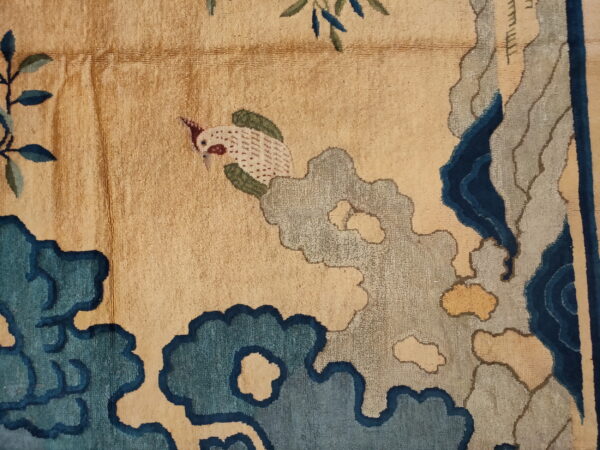 Detail shot of a tan rug featuring a bird and stylized clouds in deep blue, teal, and gray.