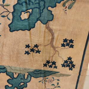 Textured tan rug with an elaborate floral, branch, and bird pattern in teal and brown.