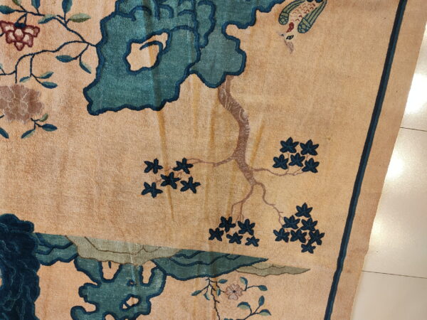 Textured tan rug with an elaborate floral, branch, and bird pattern in teal and brown.