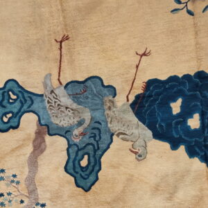 Close-up of a low pile beige rug featuring two stylized gray birds and abstract dark blue cloud designs.