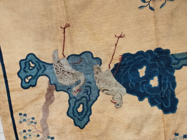 Close-up of a low pile beige rug featuring two stylized gray birds and abstract dark blue cloud designs.