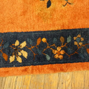 Rust orange and navy blue high-pile rug border with colorful floral vines rests on distressed wood.