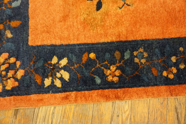 Rust orange and navy blue high-pile rug border with colorful floral vines rests on distressed wood.