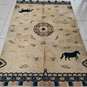 Low pile tan rug featuring navy horses, a central medallion, and elaborate fretwork borders on white tile.
