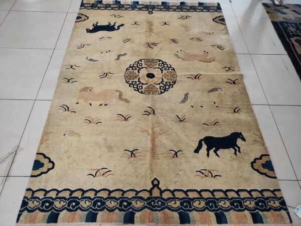 Low pile tan rug featuring navy horses, a central medallion, and elaborate fretwork borders on white tile.