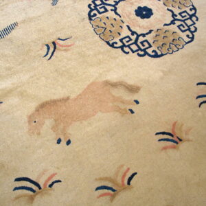 Close-up of a low-pile rug with a beige field featuring a pinkish-tan horse and dark blue motifs.