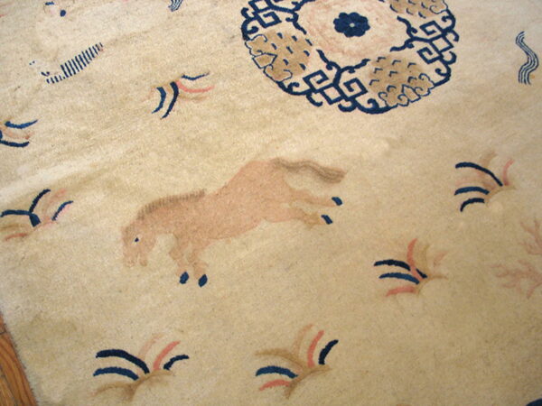Close-up of a low-pile rug with a beige field featuring a pinkish-tan horse and dark blue motifs.