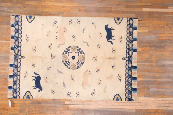Beige rug with dark blue, tan, and pink animal patterns, featuring a wide scrolled border on a wood floor.