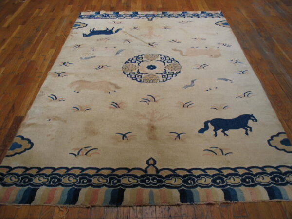 Cream field rug featuring stylized blue and light tan horses, a central medallion, and complex cloud borders on a wood floor.