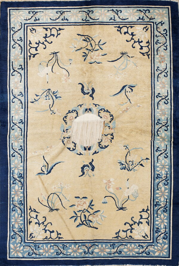 Beige rug with navy blue and light blue floral border shows severe damage exposing the white foundation.
