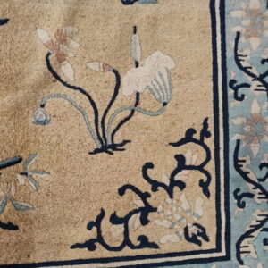 Low-pile rug detail showing a tan field with stylized blue and pink floral motifs and a complex blue border.