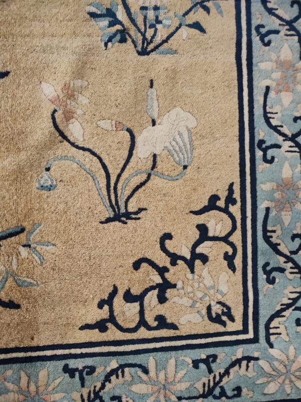 Low-pile rug detail showing a tan field with stylized blue and pink floral motifs and a complex blue border.