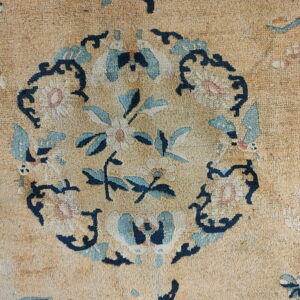Close-up detail of a low-pile tan rug featuring a central floral medallion in blue, navy, and cream.