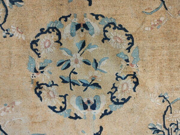 Close-up detail of a low-pile tan rug featuring a central floral medallion in blue, navy, and cream.