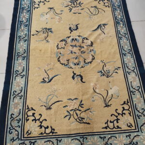 Beige rug featuring a detailed dark blue floral border and light blue botanical motifs on a white tile floor.