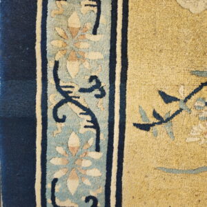 Detail of a rug showing a mustard yellow field bordered by navy and light blue floral designs.