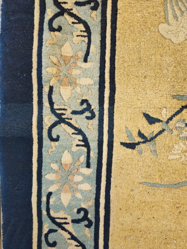 Detail of a rug showing a mustard yellow field bordered by navy and light blue floral designs.