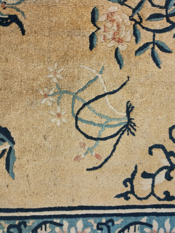 Detail of a textured tan rug showing blue and cream floral patterns and a dark blue border stripe.