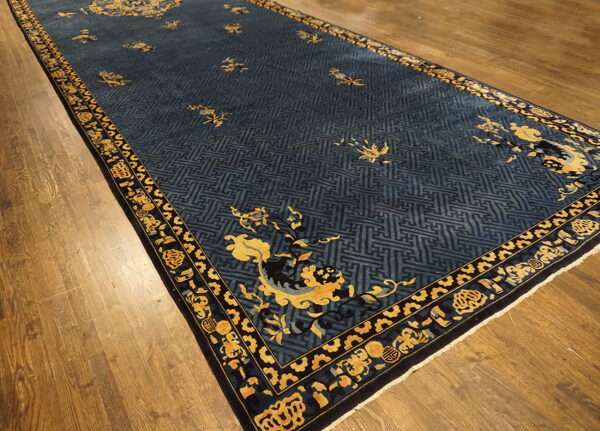 Dark blue runner rug with yellow scrollwork and geometric patterns rests on warm brown hardwood flooring.