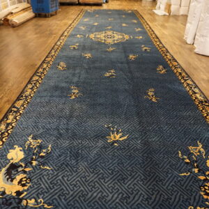 Deep blue runner rug with golden floral and medallion designs over a geometric pattern on wood flooring.
