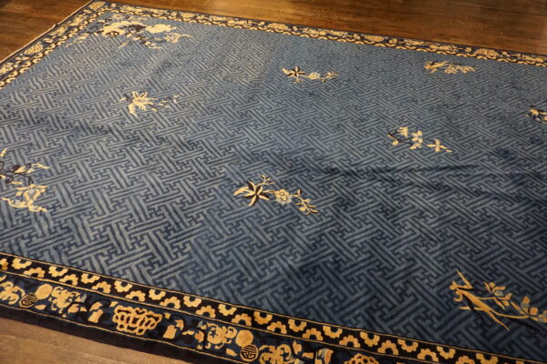 Indigo and light blue rug with a geometric fret pattern, gold floral accents, and detailed borders on dark hardwood.