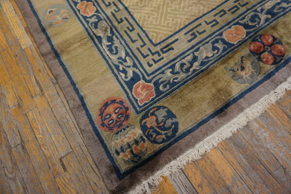 Geometric and floral patterned rug corner showing olive green, navy, and peach colors on rustic wood planks.