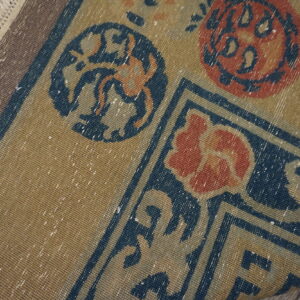 Low-pile tan rug with detailed navy and rust floral patterns and visible white fringed edge.